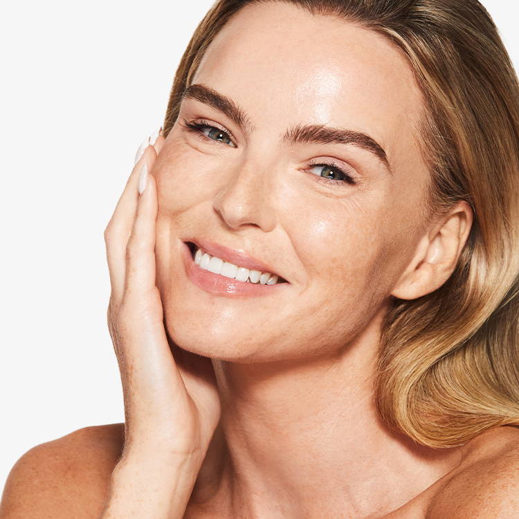 Woman with smooth skin touching her face against a plain background