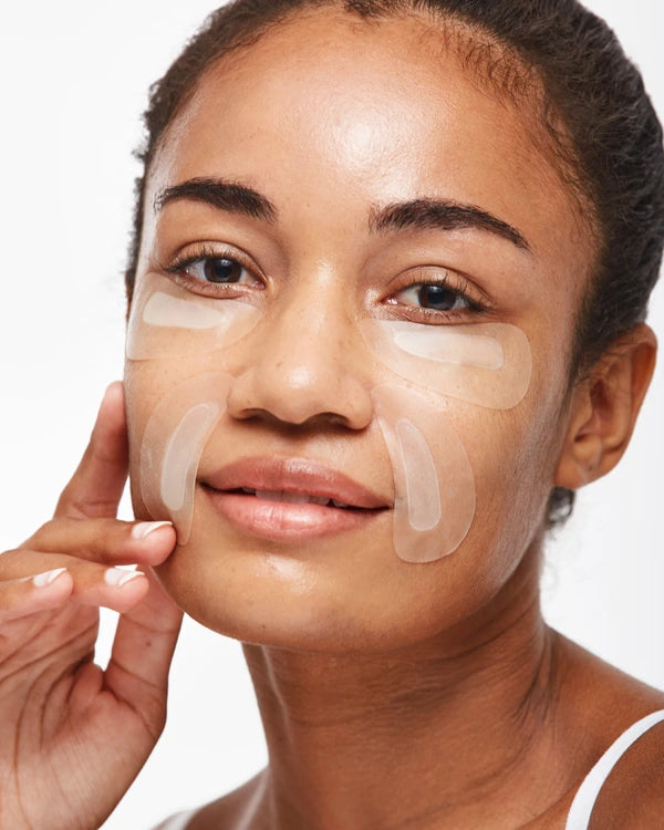 Woman applying under-eye patches on a white background
