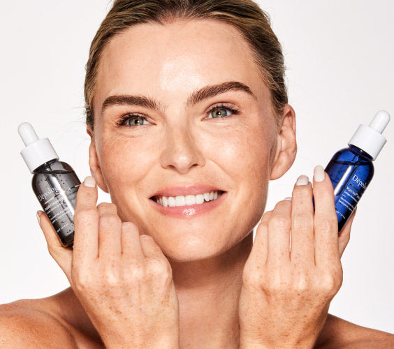 Woman holding two skincare droppers with a plain background